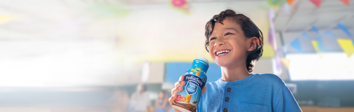 Boy drinking Chocolate PediaSure® shake with vitamins and other nutrients to help him grow.