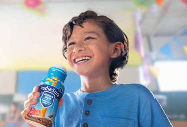 Boy drinking Chocolate PediaSure® shake with vitamins and other nutrients to help him grow.